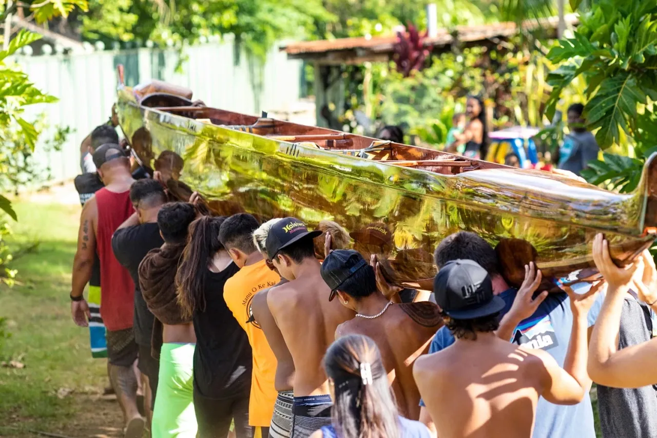 Club members carrying a hand-carved koa canoe on their shoulders